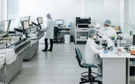 Medicinsk laboratoriemiljö med forskare i skyddskläder som analyserar prover och arbetar med mikroskop, symbol för läkemedelsforskning kopplad till novo nordisk aktie.