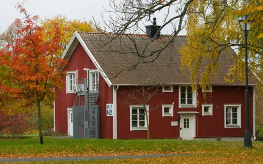 Samhällsfastighet i form av rött bostadshus i nordisk miljö med höstlöv, symbol för fastighetsinnehav och offentlig verksamhet kopplat till sbb aktie.